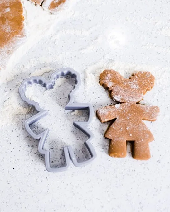 The gray Gingerbread Diva cookie cutter beside a freshly cut Diva cookie on a floured counter