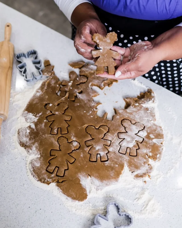 Hands hold up a Diva cookie above rolled gingerbread dough cut into Diva shapes